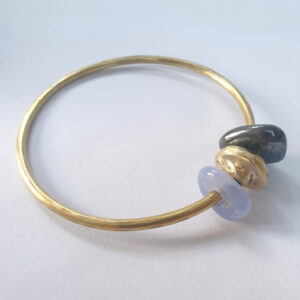 Brass Circle Bangle with three small pebble shaped beads, On one dark gemstone, one brass, one light blue gemstone.